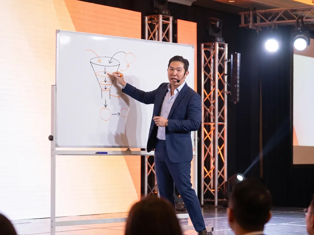 Aaron Chong drawing a sales funnel on a whiteboard in front of an audience